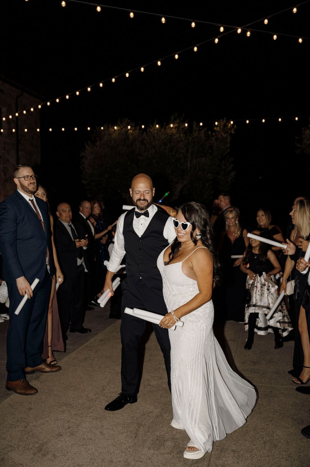 Couples dancing at night under string lights at an outdoor wedding reception.