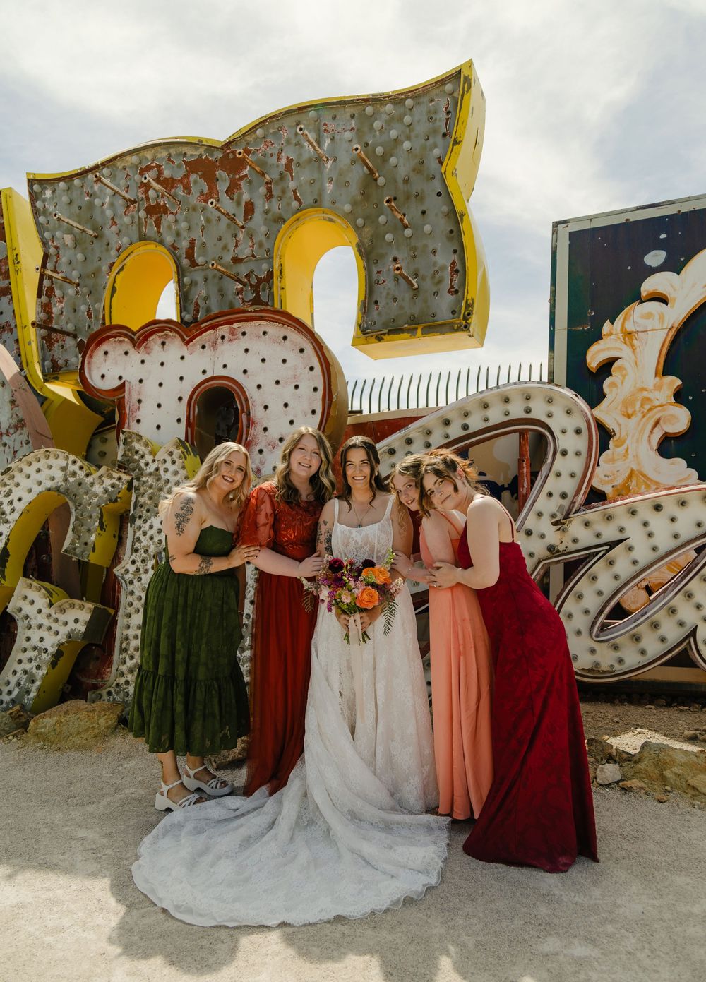 Bride and bridesmaids in colorful dresses pose before vintage neon signs at the Neon Museum in Las Vegas.