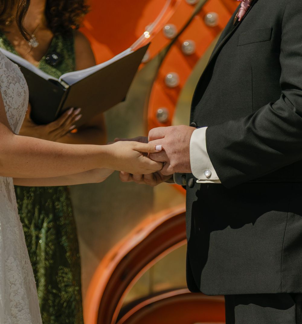 Couple exchanging rings during wedding ceremony with officiant holding book in background.