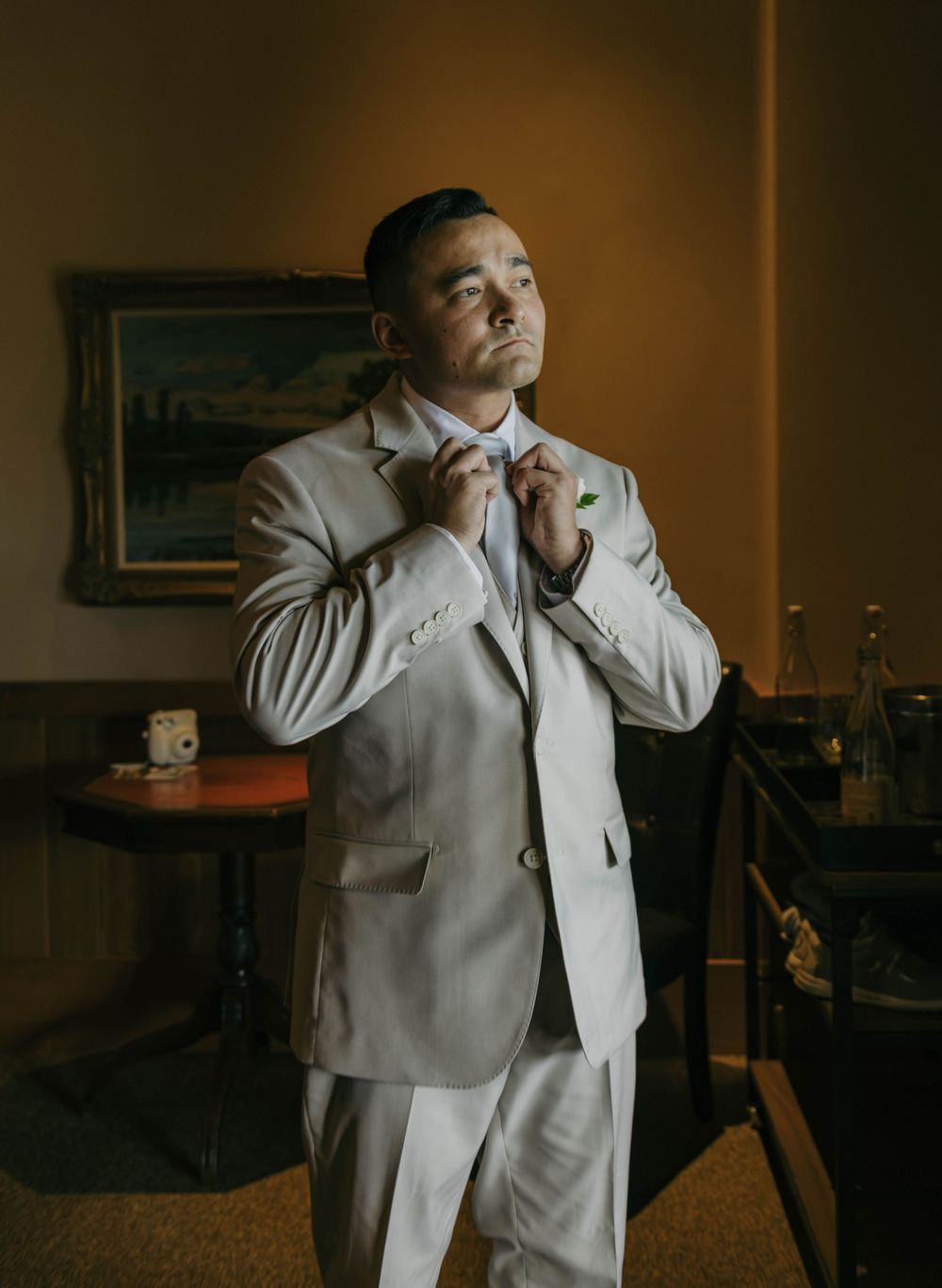 Groom in a light beige suit adjusting his bow tie before the wedding ceremony.