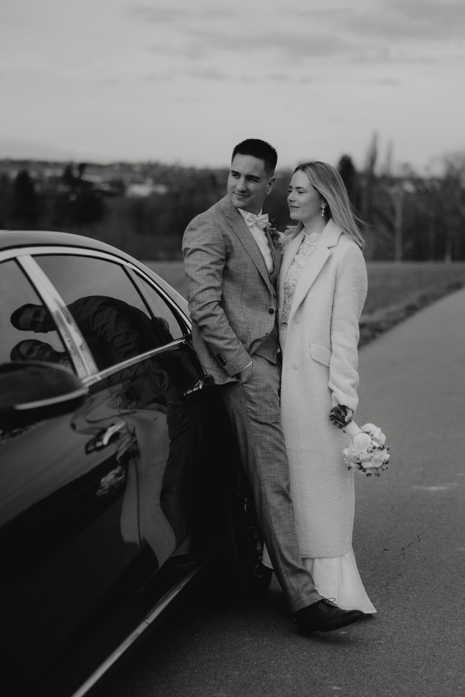 Elegant couple poses against a vintage car in formal winter attire.
