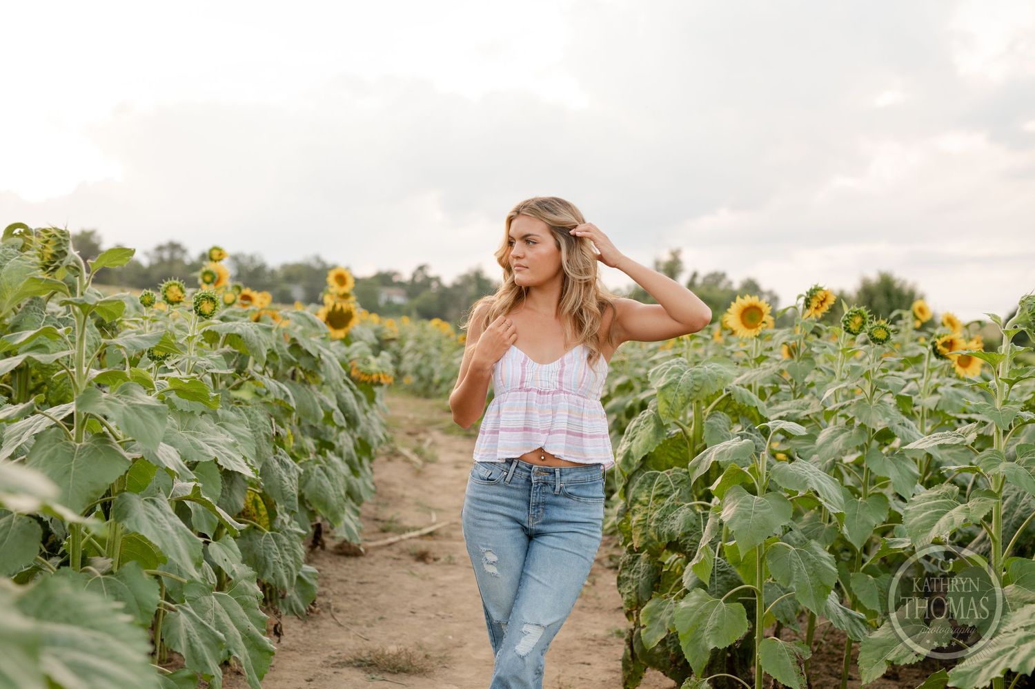 A stylish summer photoshoot among tall sunflower plants on a dirt path.