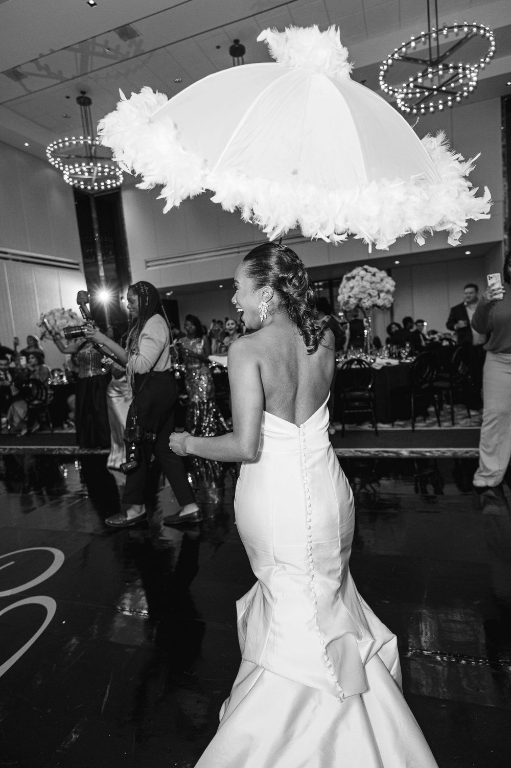 A graceful white wedding gown silhouetted against decorative parasols and elegant chandeliers.