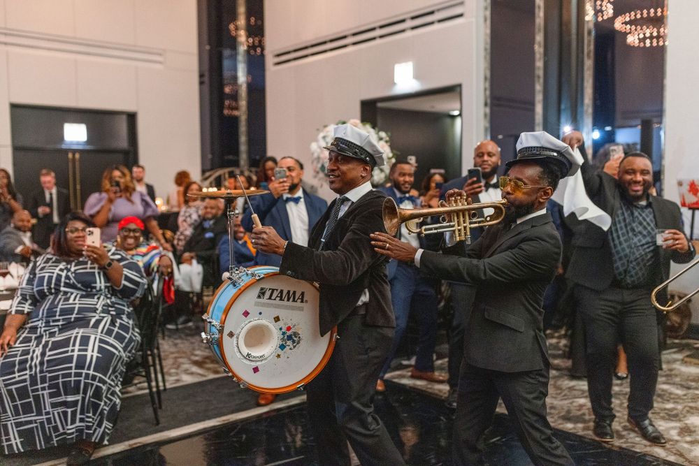 A vibrant brass band performs at a wedding reception wearing traditional New Orleans style attire.