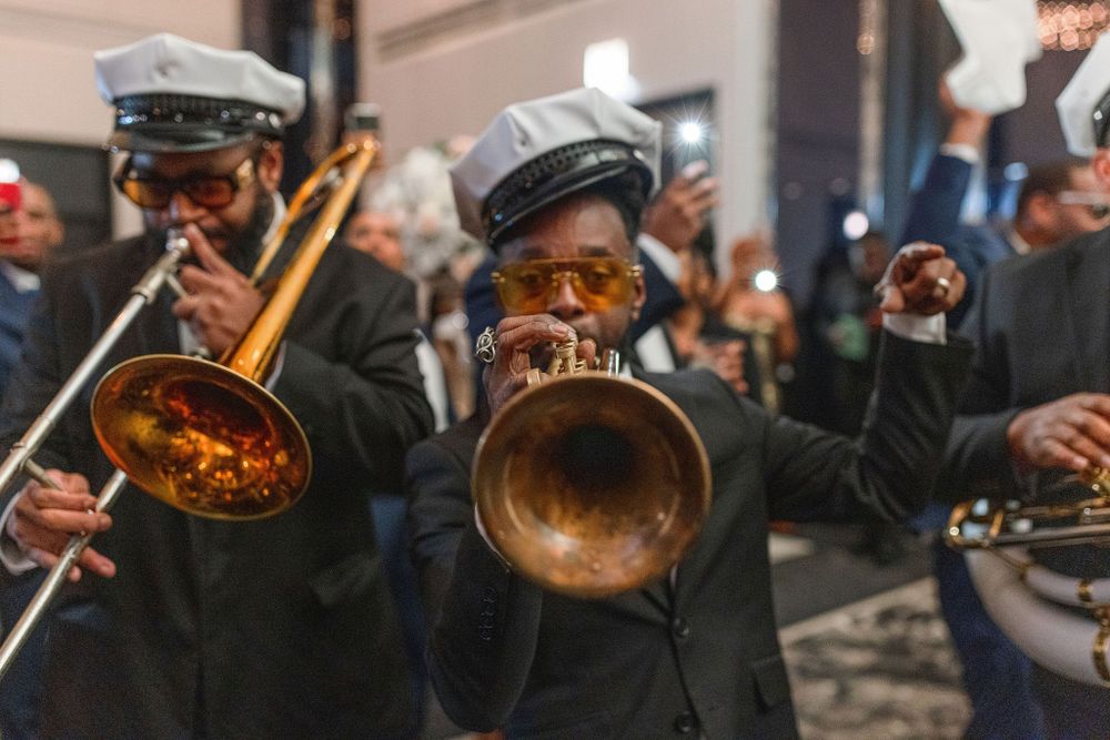 Brass band musicians play trumpets and trombones while wearing traditional navy caps.