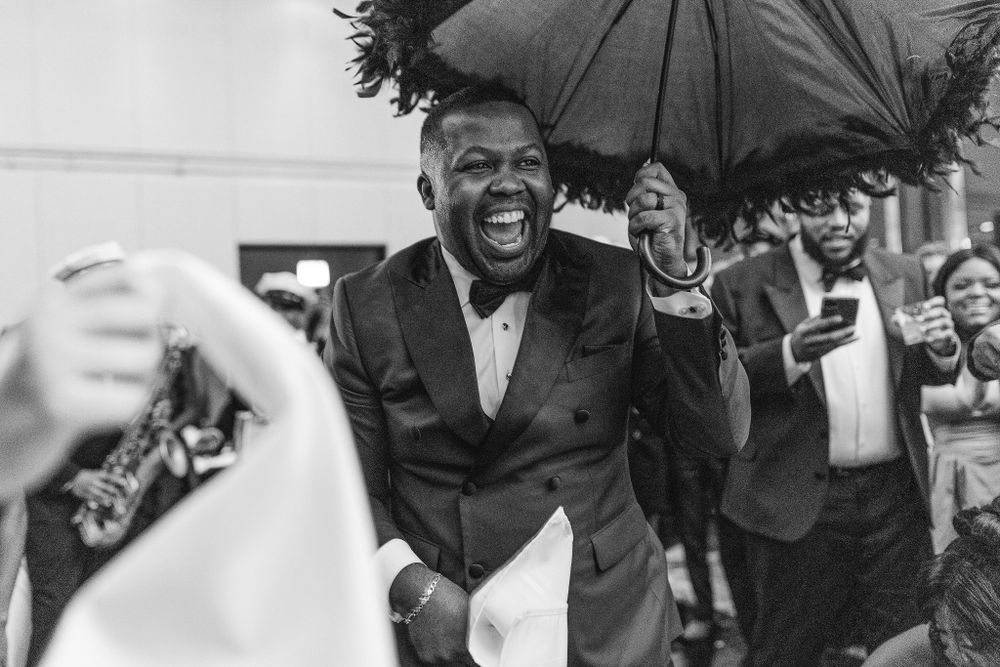 Black and white photo showing joyful celebration with parasol at formal event.