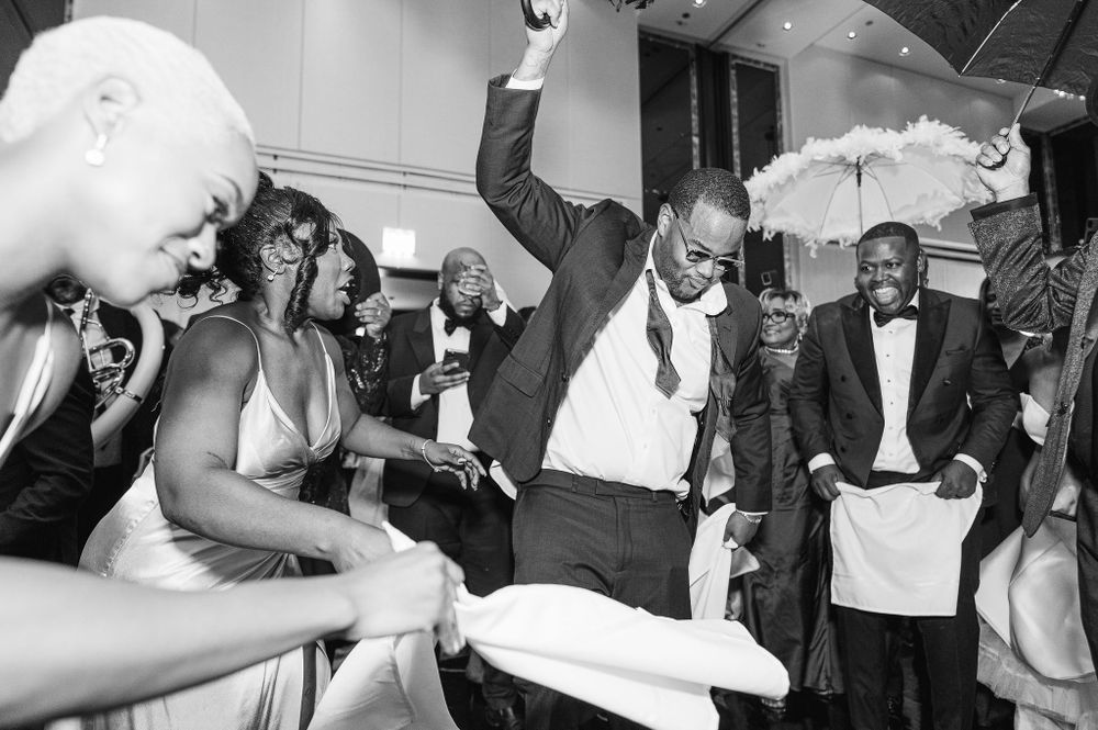 Guests at a wedding reception dance energetically in black and white formal attire while celebrating joyfully.