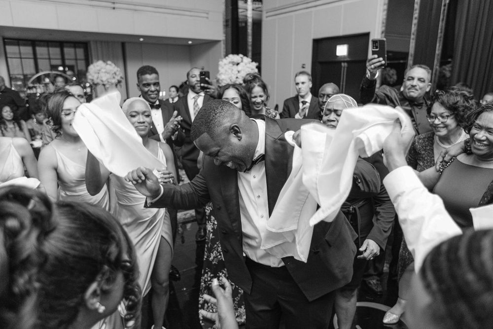 Black and white photo of wedding guests dancing and waving handkerchiefs at a lively reception.