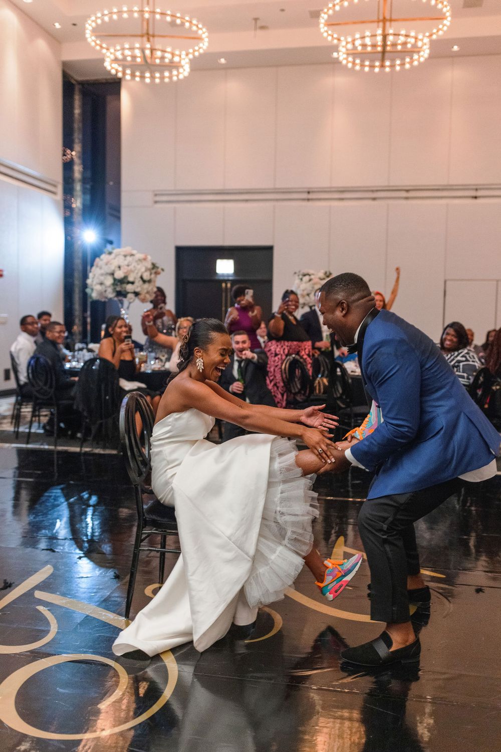 Couple dancing together on an elegant ballroom floor with illuminated chandeliers overhead.