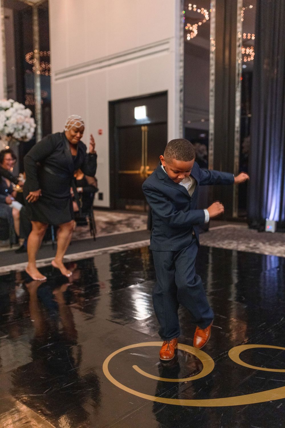 Wedding guest performs dance moves on a shiny black floor with decorative gold circles.