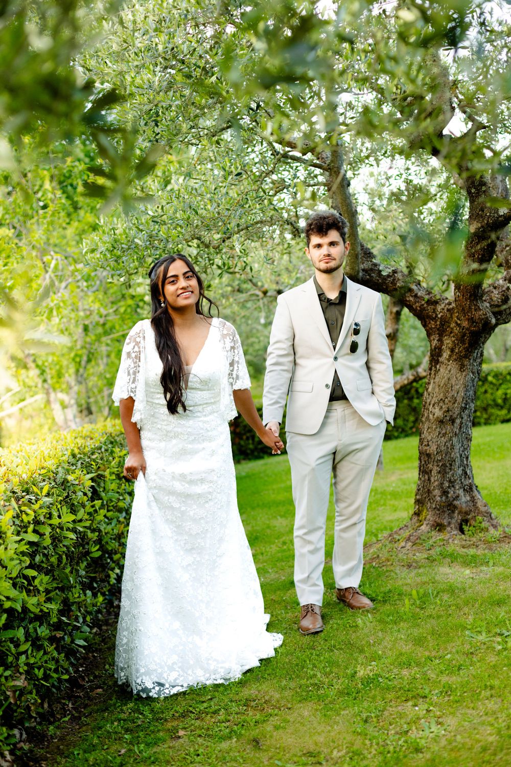Newlyweds share intimate wedding photos among olive trees in Italian garden setting.
