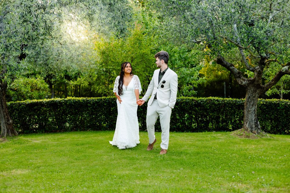 Romantic wedding couple captured in distance walking through verdant Italian garden.
