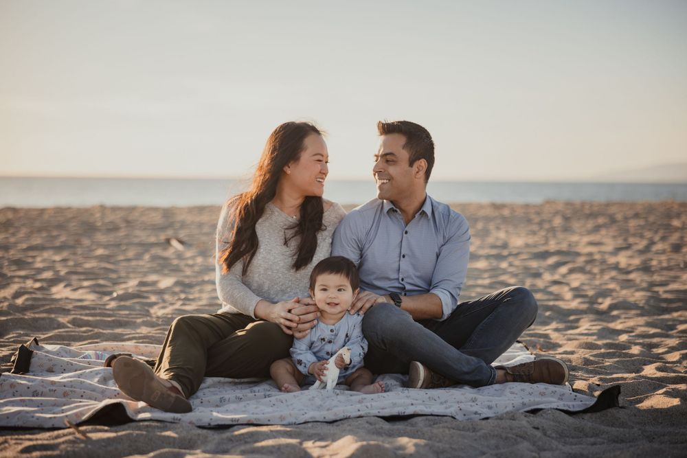A family sits together on a beach blanket during sunset for a casual photo session.