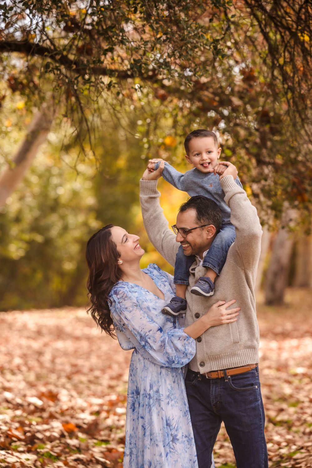Family playing and laughing together among fallen autumn leaves in park setting.