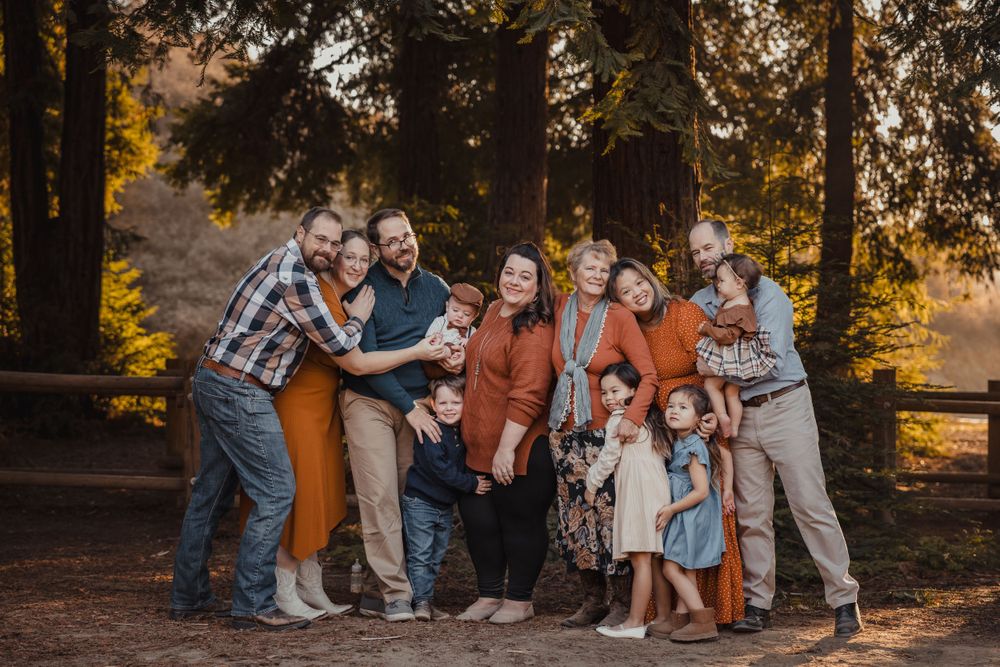 Large family group posing together outdoors during golden hour in autumn forest setting.