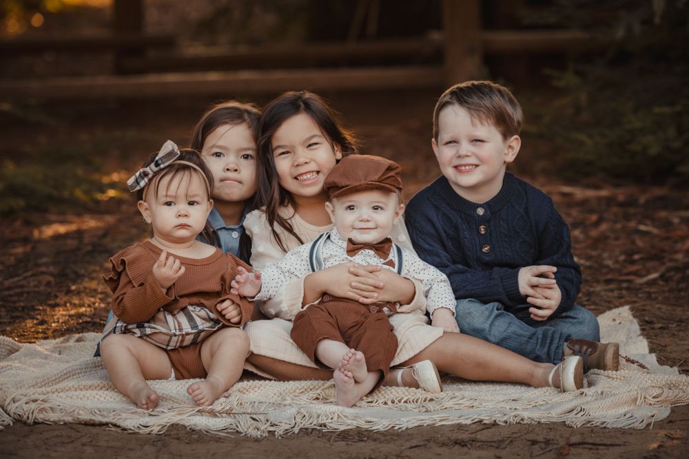 Children sitting together on white blanket during autumn outdoor photo session.