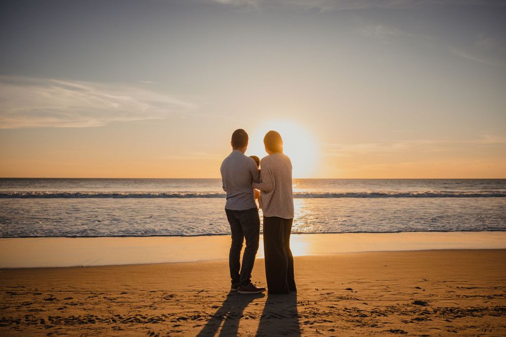 Two people stand silhouetted against a golden sunset on the beach.