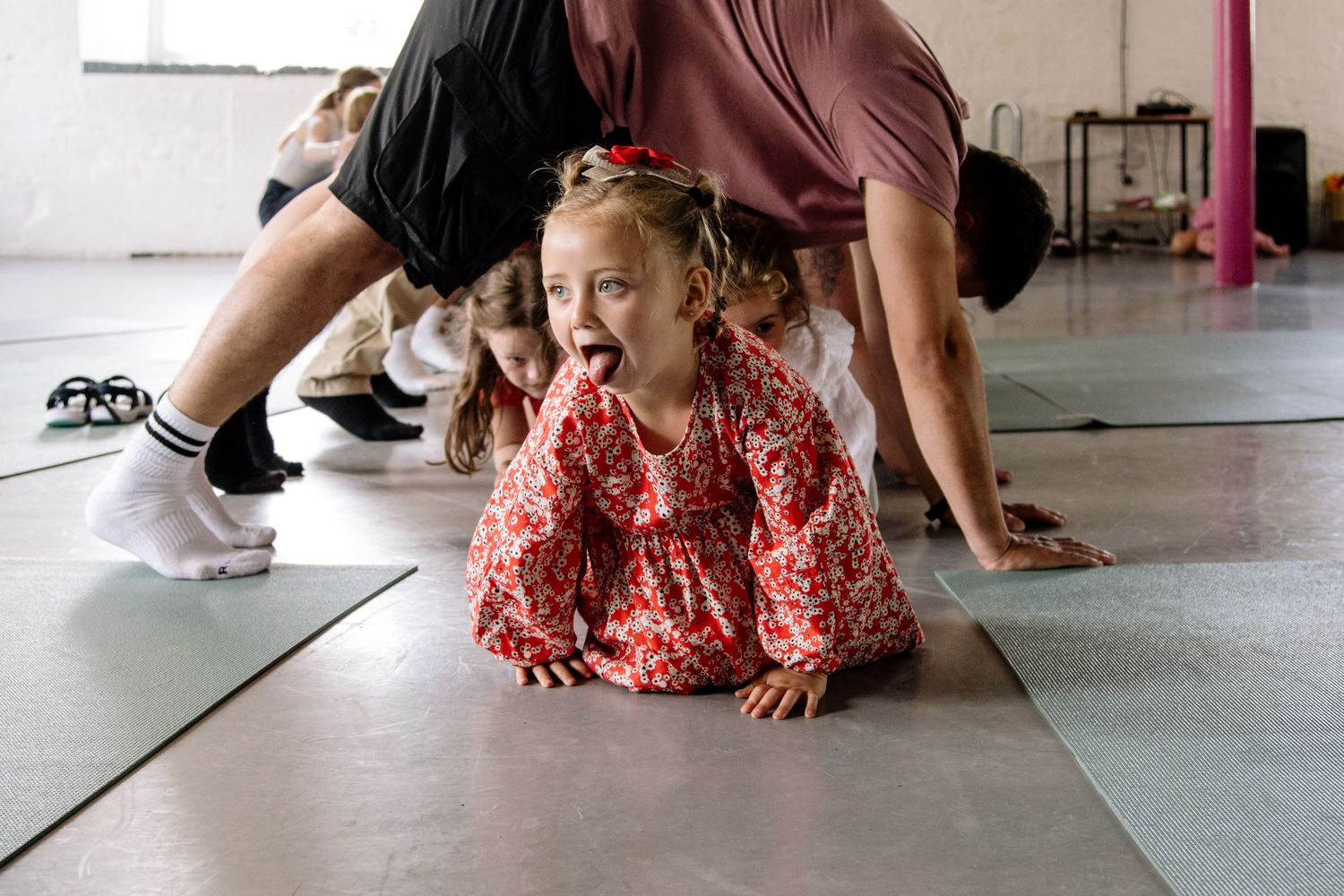 A dancer in a red floral dress practices movements on a studio floor.