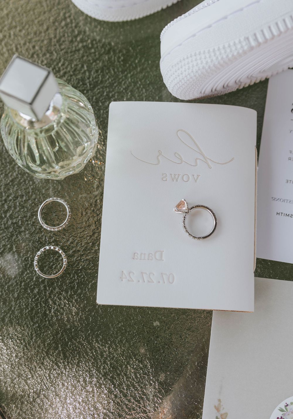 Wedding stationery flatlay featuring engagement ring, wedding bands and crystal perfume bottle.
