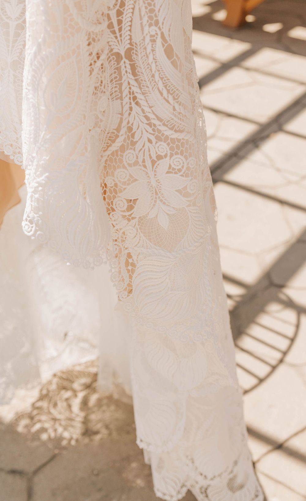 Delicate lace detail of a white wedding dress with intricate floral patterns in sunlight.