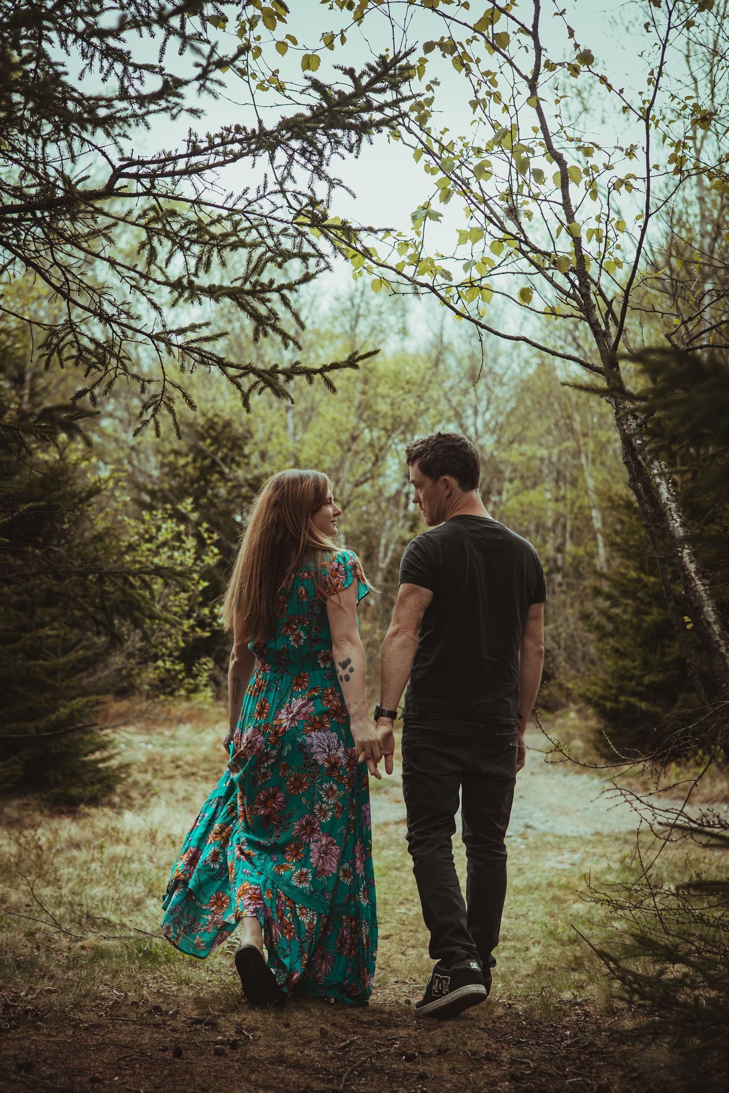 Two people strolling hand in hand along a wooded trail.