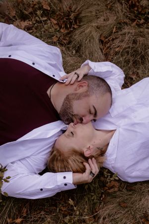 Couple lying on ground sharing intimate moment in white button-up shirts.