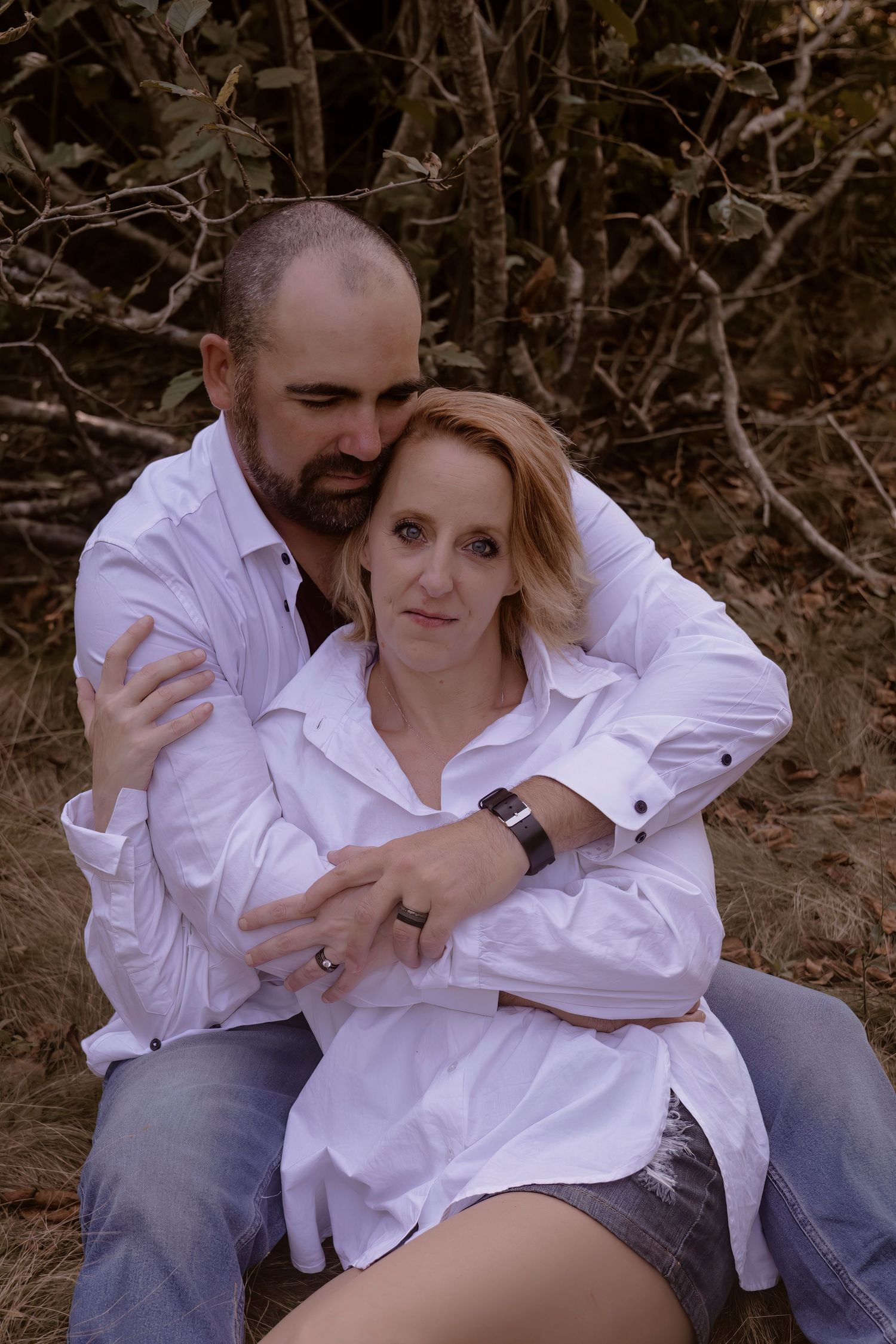 Couple in white shirts embracing outdoors in casual romantic portrait.