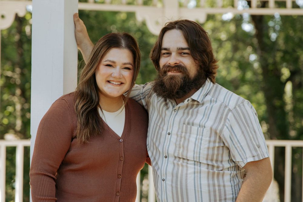 A couple poses together under a white gazebo wearing casual attire.