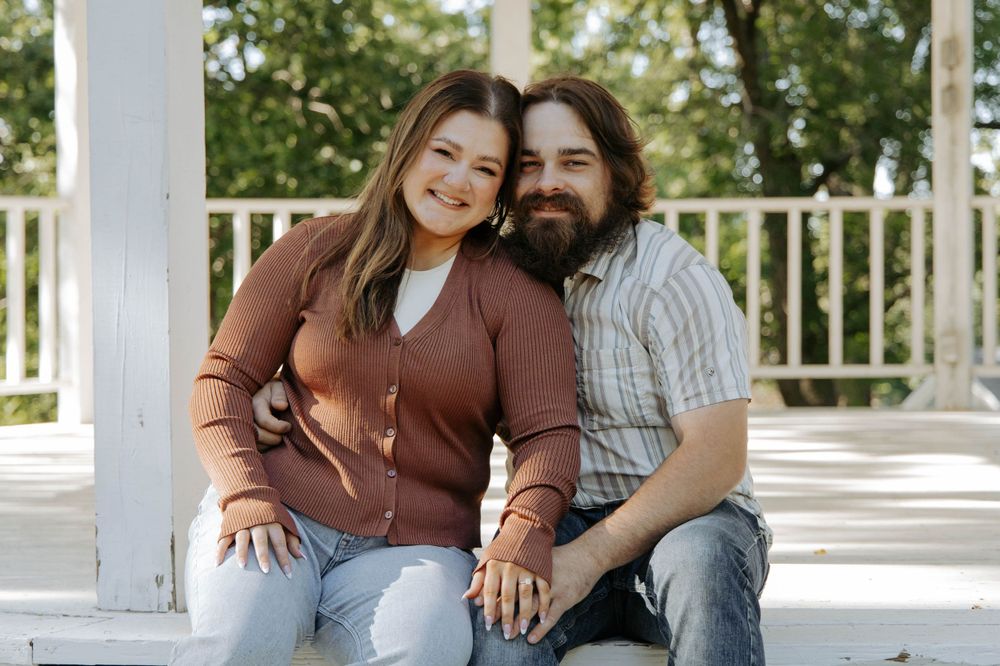 A couple sits close together on white gazebo steps sharing a tender moment.