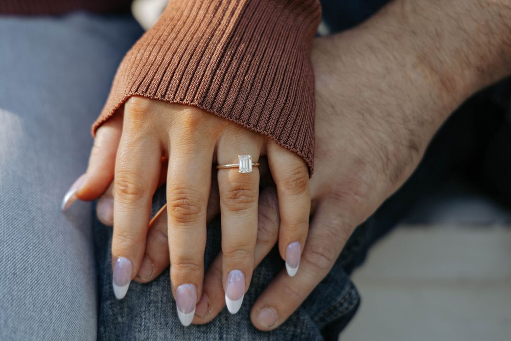 Two hands intertwined showing an engagement ring against a cozy sweater background.