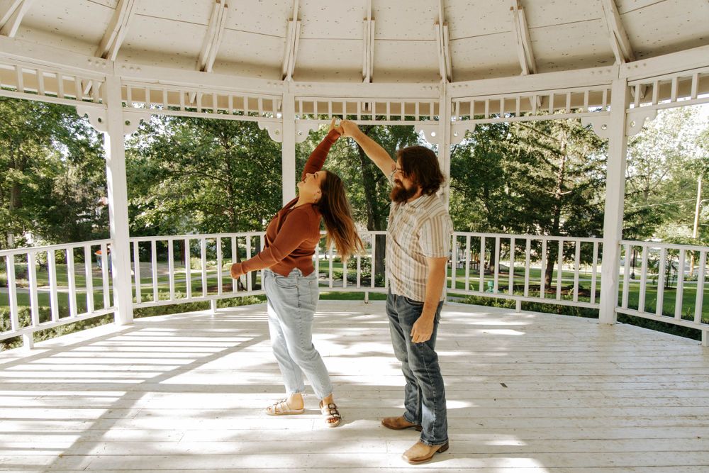 A couple dances together in a white gazebo surrounded by greenery on a sunny day.