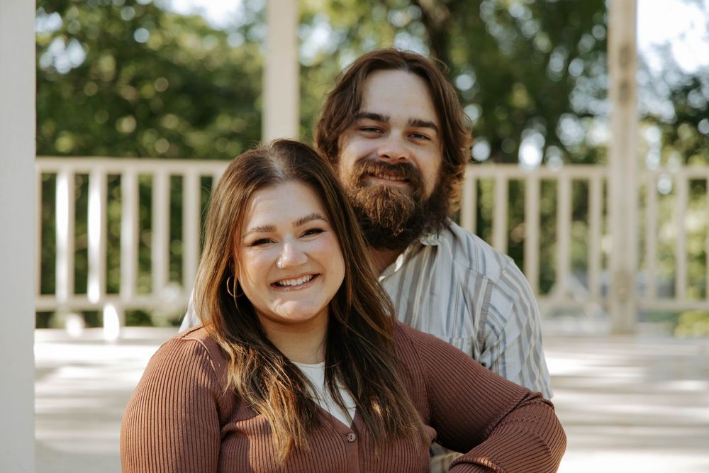 A couple smiles warmly while embracing in a white gazebo setting.