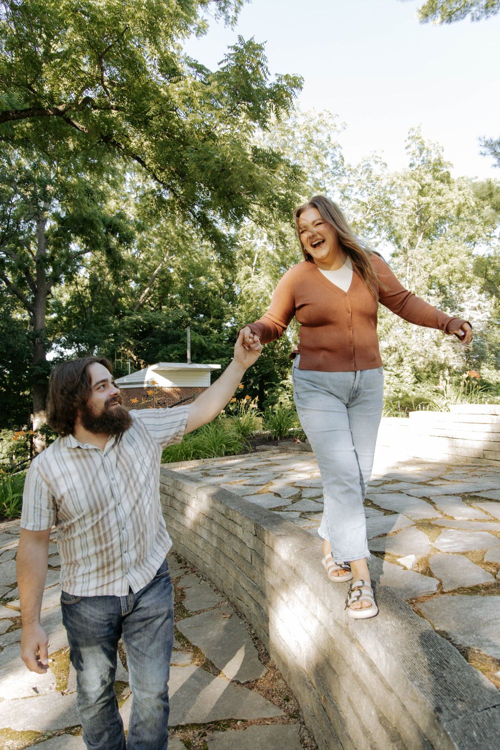 A couple enjoys a playful moment outdoors with one person balancing on stone steps.