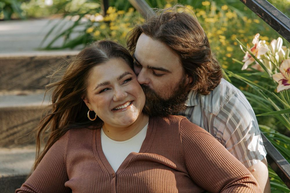 A couple shares a tender moment on outdoor steps surrounded by yellow flowers.