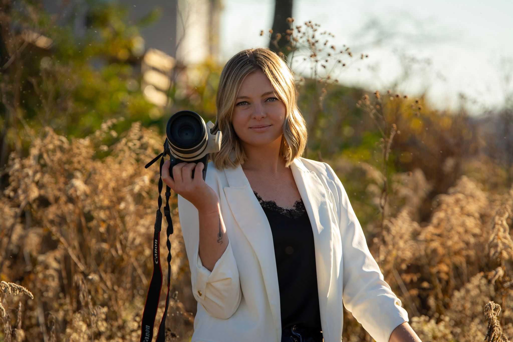 Professional photographer in white blazer holding camera during golden hour photoshoot.