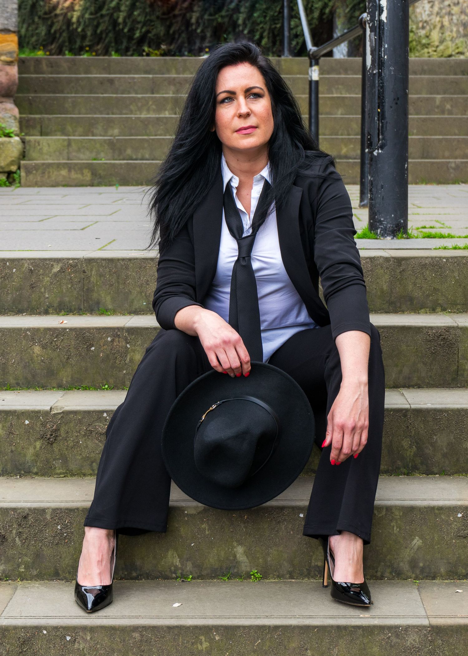 Person in black suit and white shirt poses seated on concrete steps.