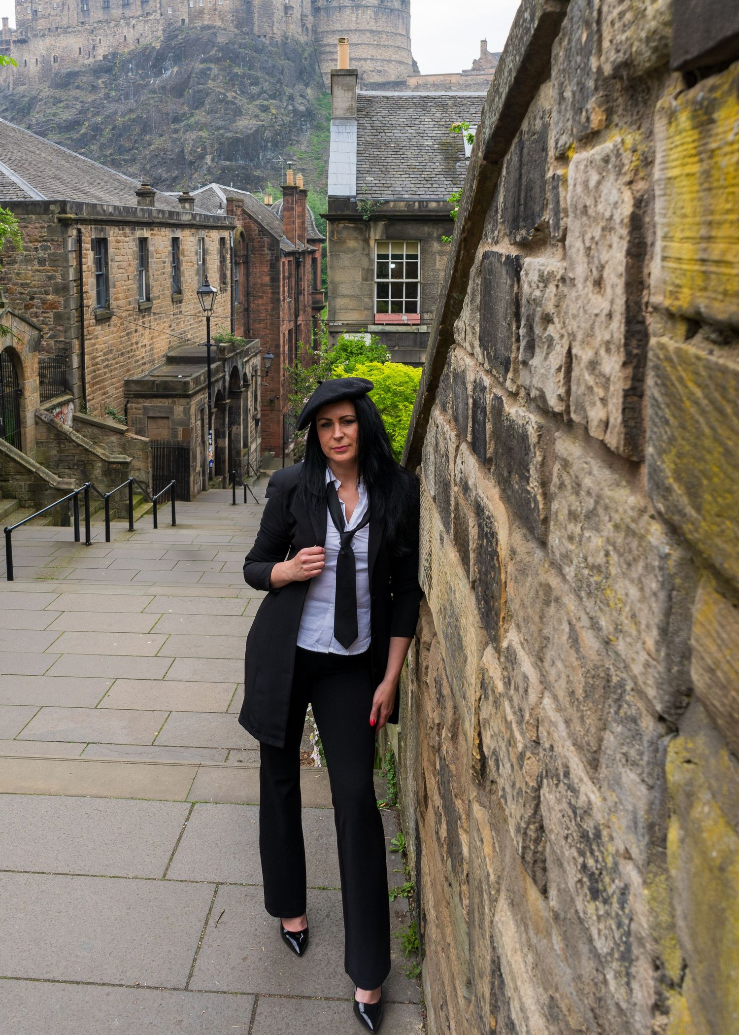 Person in black suit walks along stone wall pathway in historic district.