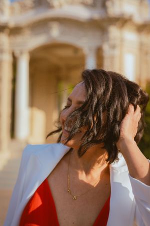 Candid shot of woman in white blazer touching her hair with sunlit architecture in background.