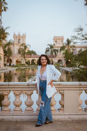 Elegant pose by reflecting pool with Spanish colonial architecture and palm trees in background.
