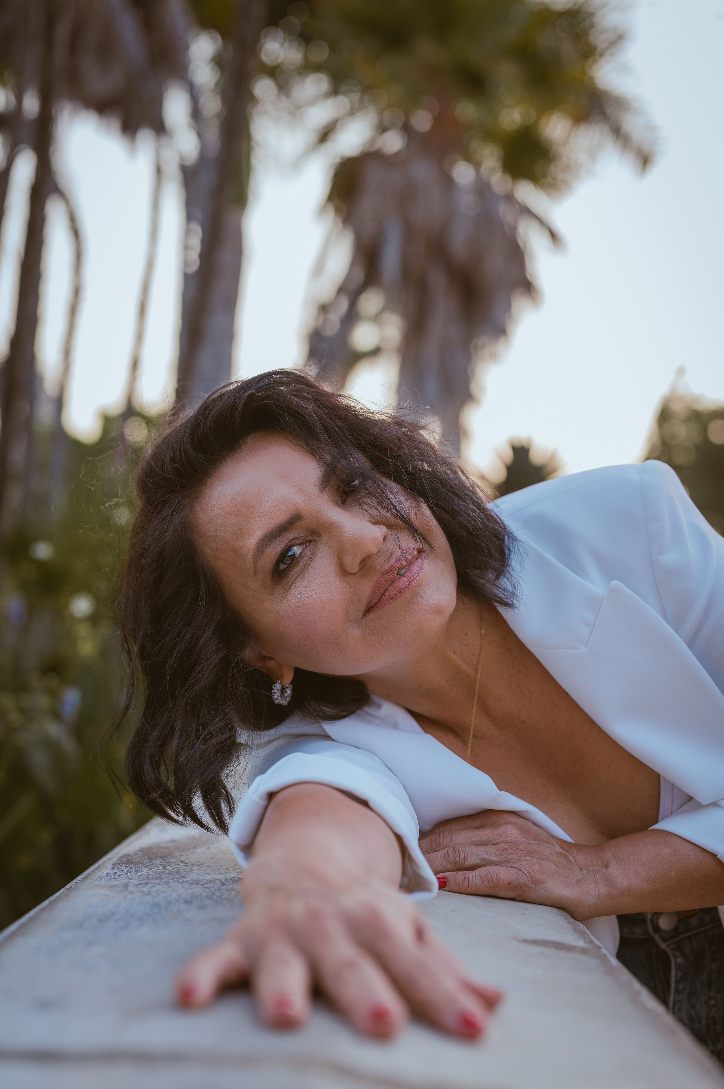 Woman in white clothing lying down in a dreamy outdoor photoshoot with palm trees in background.