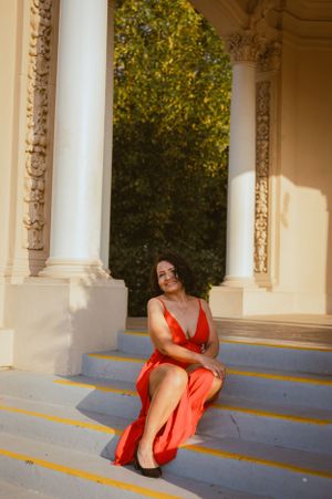 Woman in red dress sits gracefully on steps of classical building with ornate columns.