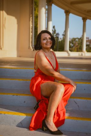 Woman in vibrant red dress poses joyfully on blue-painted steps of historic building.