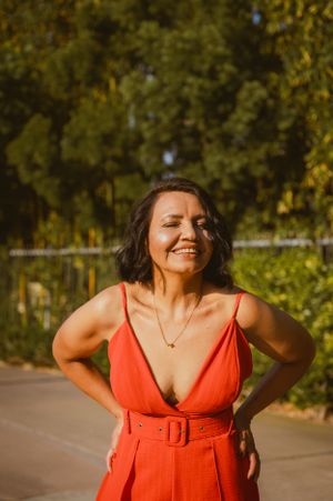 Woman in coral dress stands confidently against lush garden background in golden sunlight.