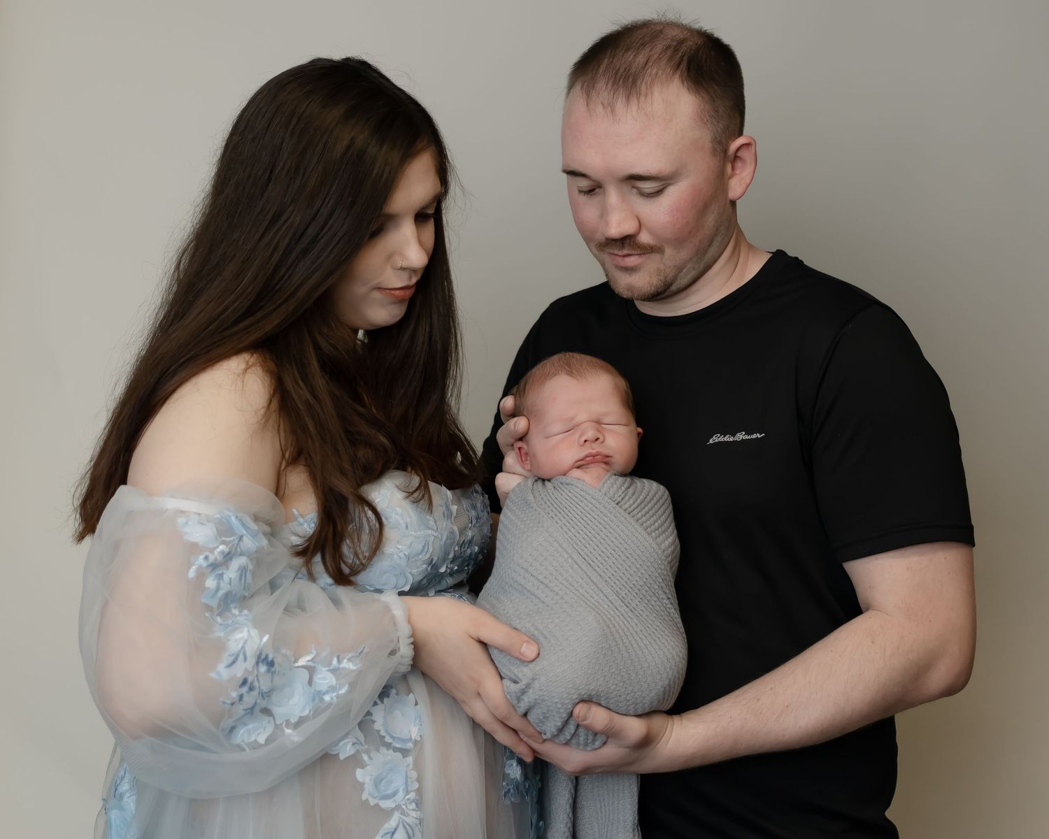 A studio portrait featuring a newborn baby with parents.