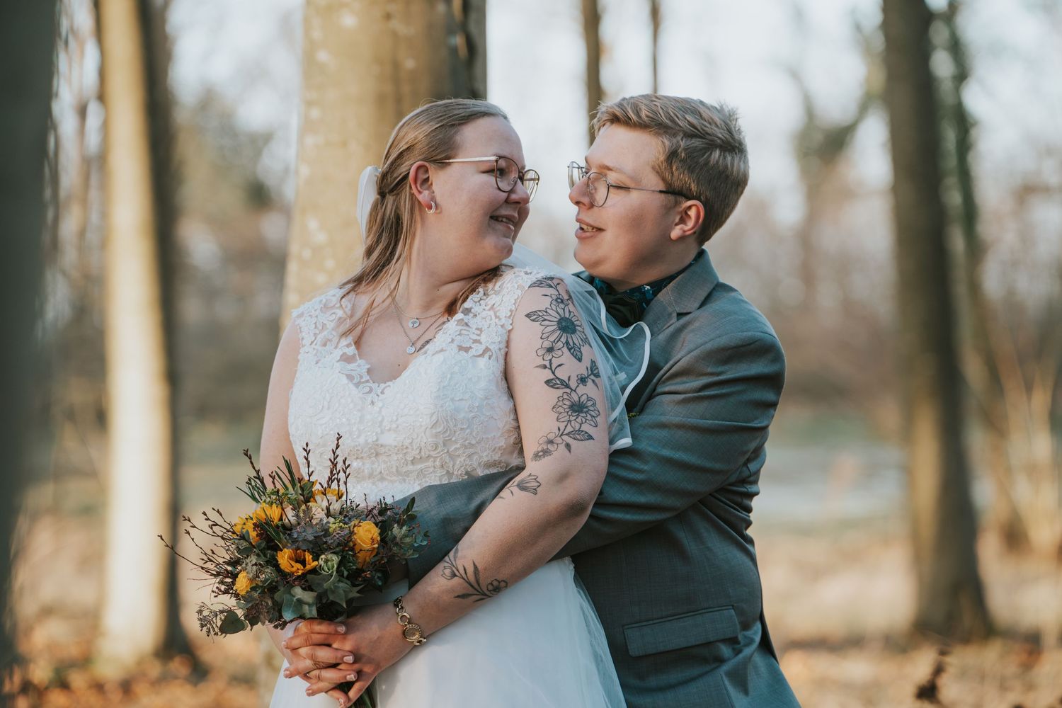 Autumn wedding portrait with couple embracing among bare trees in golden afternoon light.