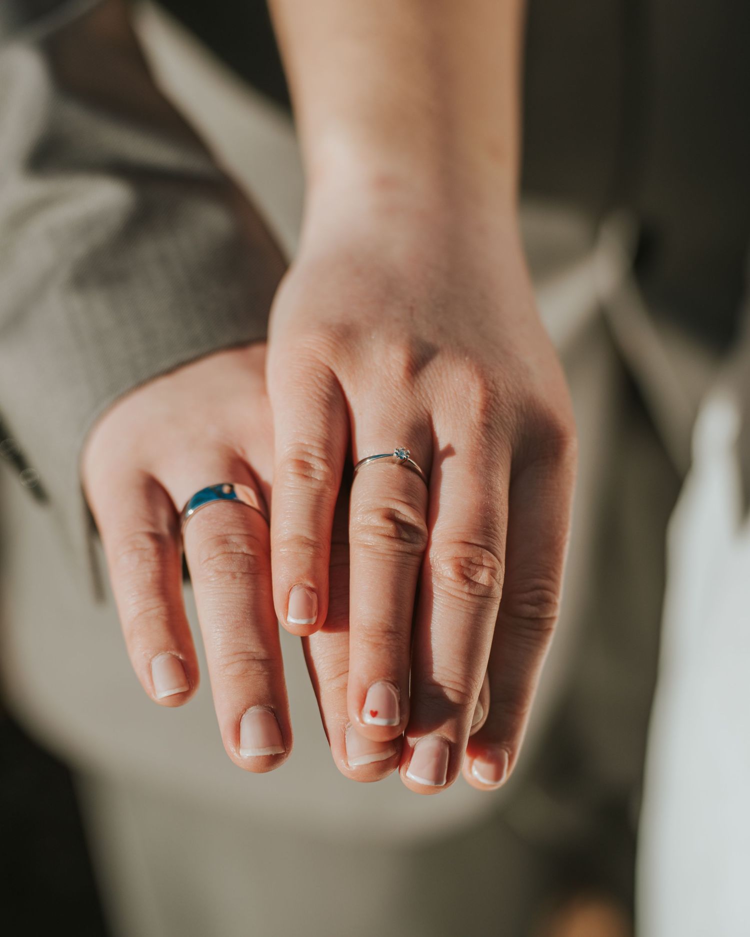 Close-up view of hands wearing wedding rings and simple nail polish.