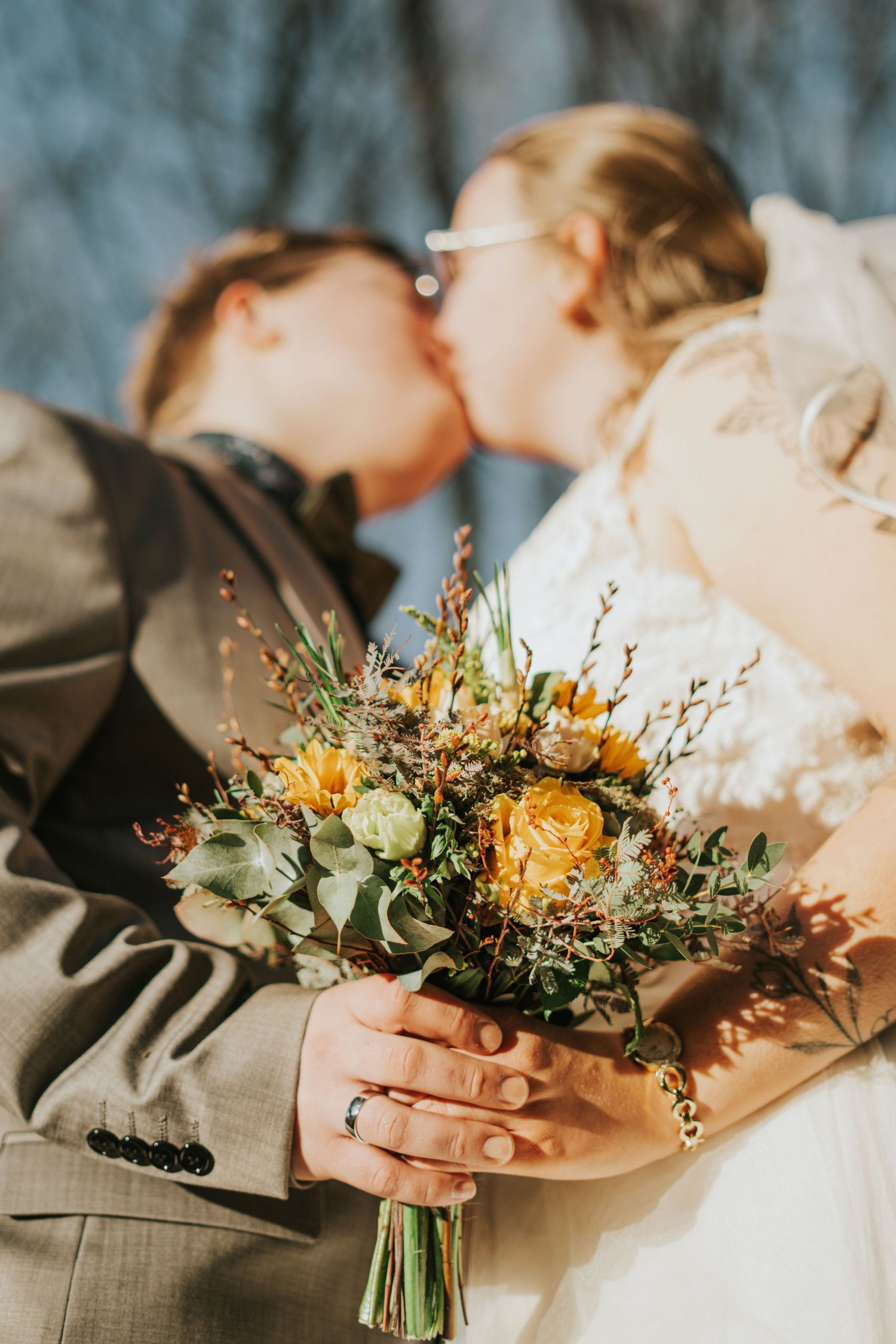 Wedding bouquet with yellow flowers and greenery held against sunlit background.
