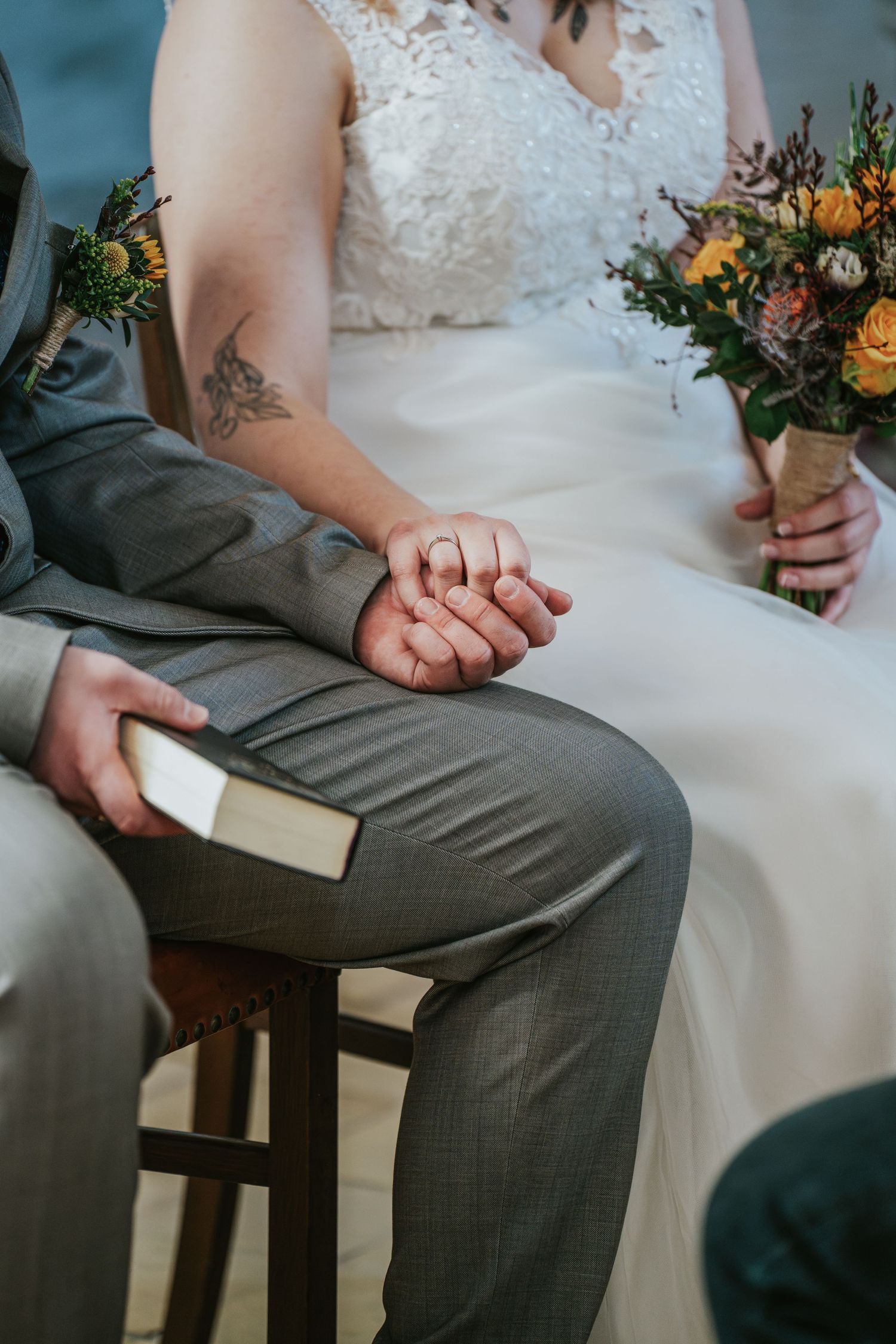 Close-up of hands holding a bouquet while sitting in formal wedding attire.
