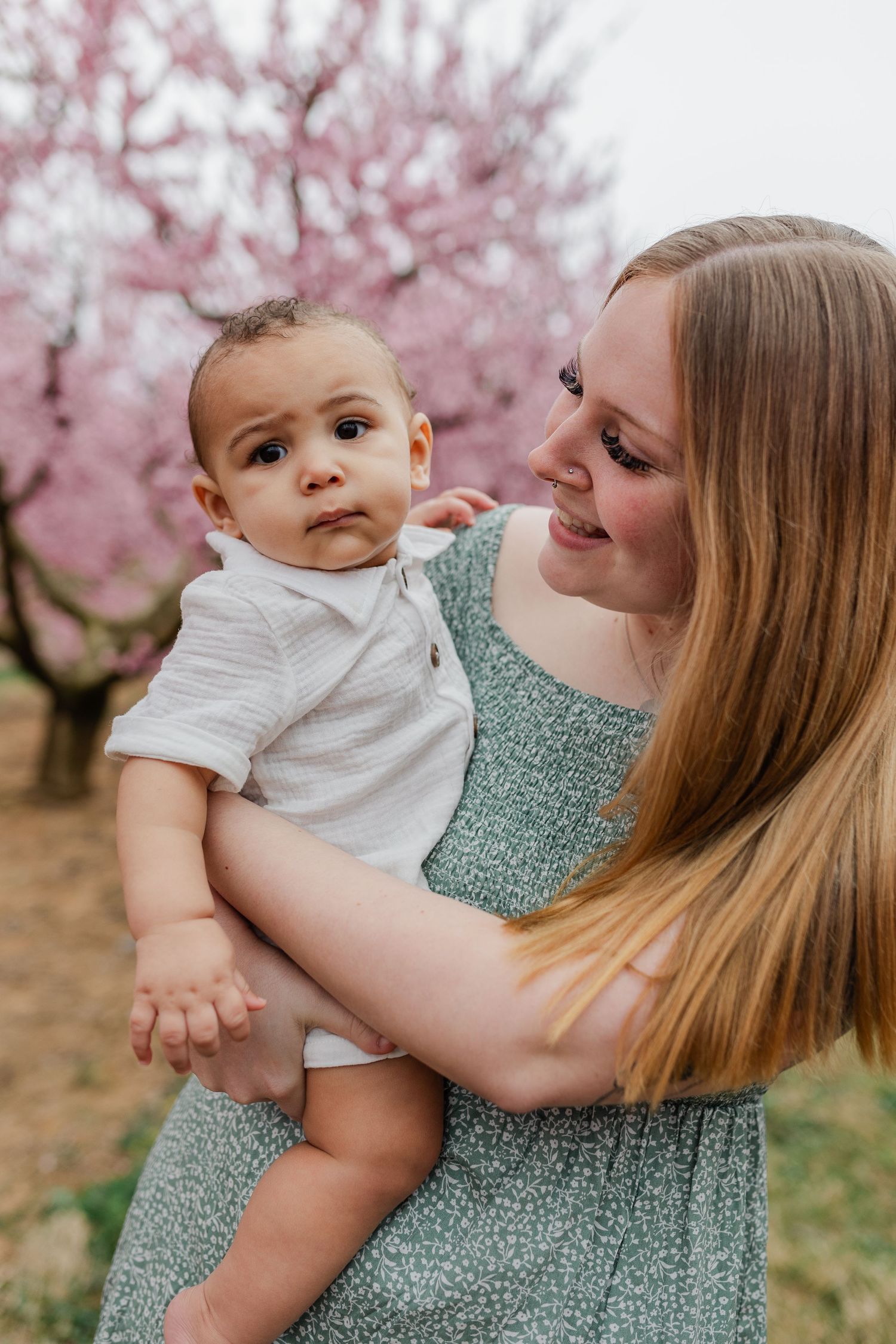 A tender moment captured under blooming cherry blossoms with a sage green dress against a soft pink spring backdrop.