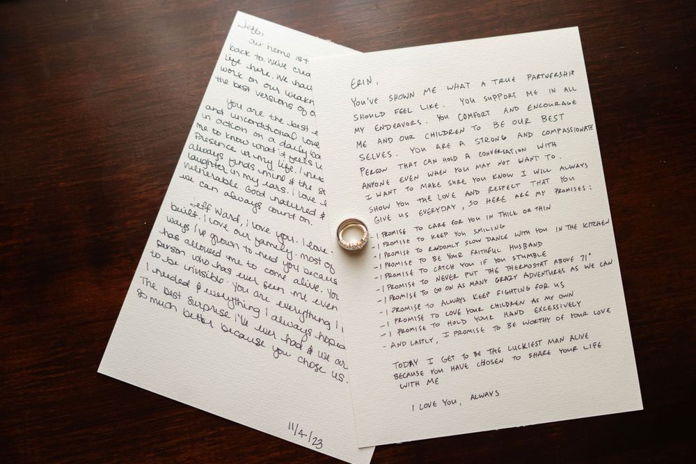 Handwritten wedding vow letters on white paper with gold wedding band ring on wooden table.